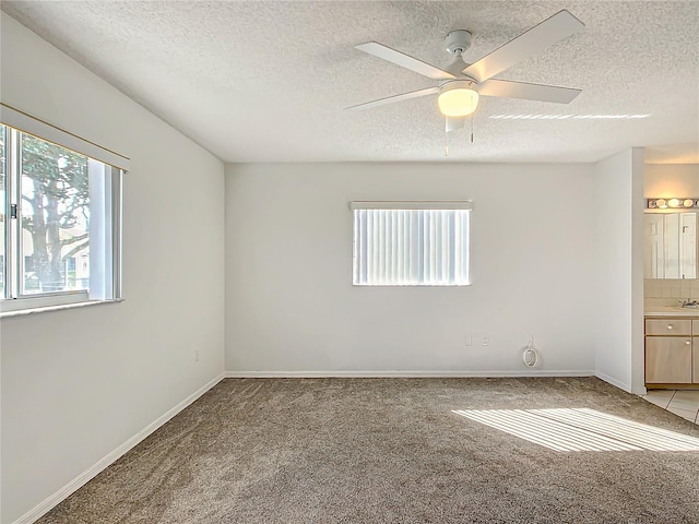 empty room featuring light carpet, ceiling fan, a textured ceiling, and baseboards