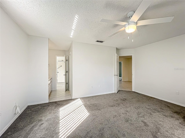 unfurnished room with a textured ceiling, ceiling fan, light colored carpet, visible vents, and baseboards