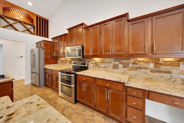 6307 SE 8th Ln, Ocala, FL 34472 - kitchen featuring appliances with stainless steel finishes, tasteful backsplash, light stone countertops, high vaulted ceiling, and brown cabinetry