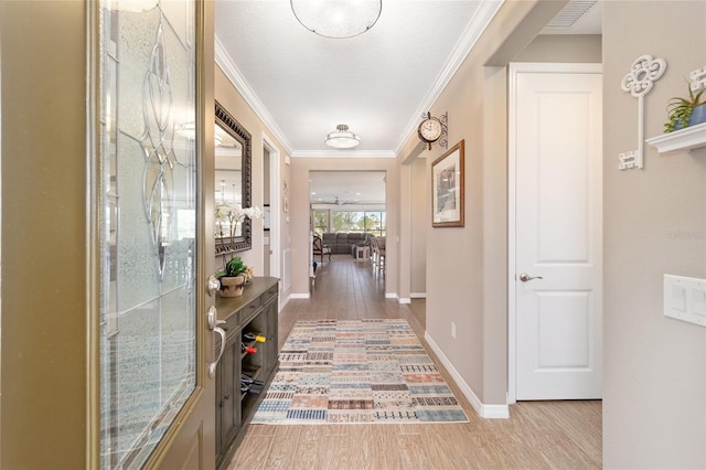 corridor featuring visible vents, baseboards, wood finished floors, and crown molding