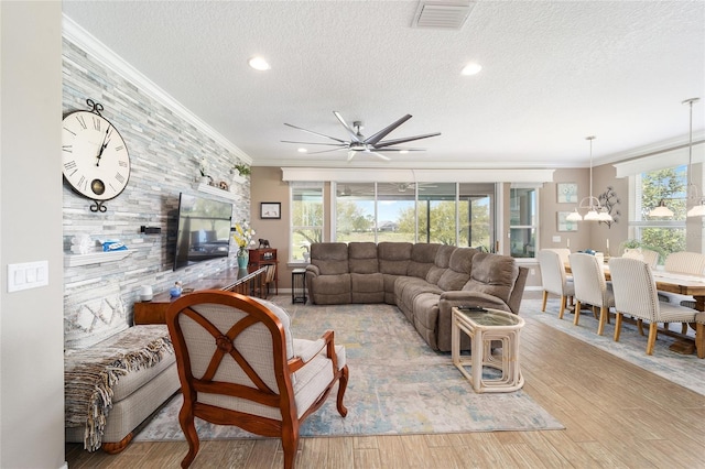 living area featuring a ceiling fan, visible vents, light wood-style floors, a textured ceiling, and crown molding