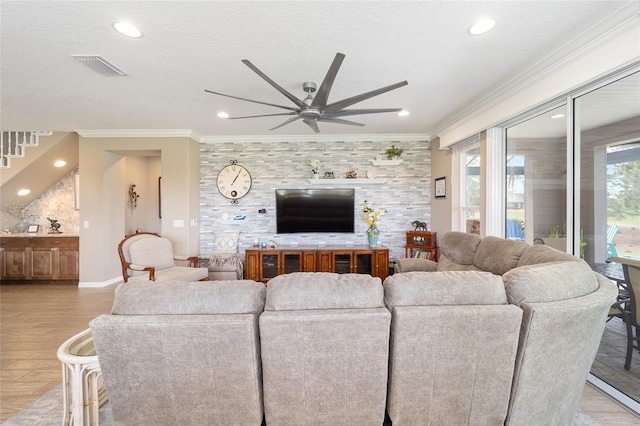 living room featuring visible vents, light wood finished floors, ceiling fan, a textured ceiling, and crown molding