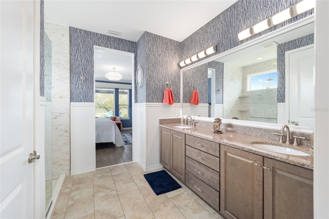 ensuite bathroom with wallpapered walls, wainscoting, and a sink