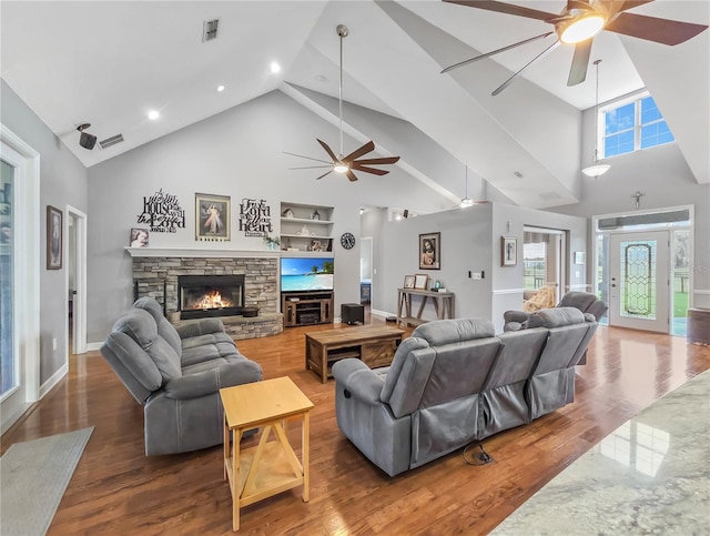 living area featuring built in shelves, a ceiling fan, a stone fireplace, and wood finished floors