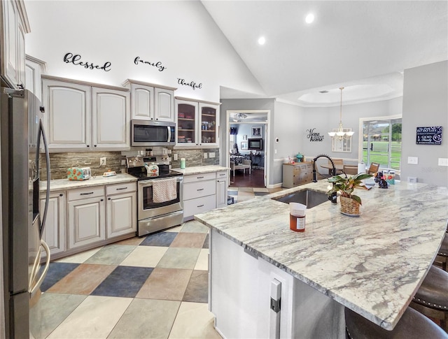 kitchen with light stone counters, stainless steel appliances, a breakfast bar, a sink, and backsplash