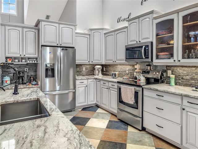 kitchen with stainless steel appliances, a sink, visible vents, decorative backsplash, and glass insert cabinets