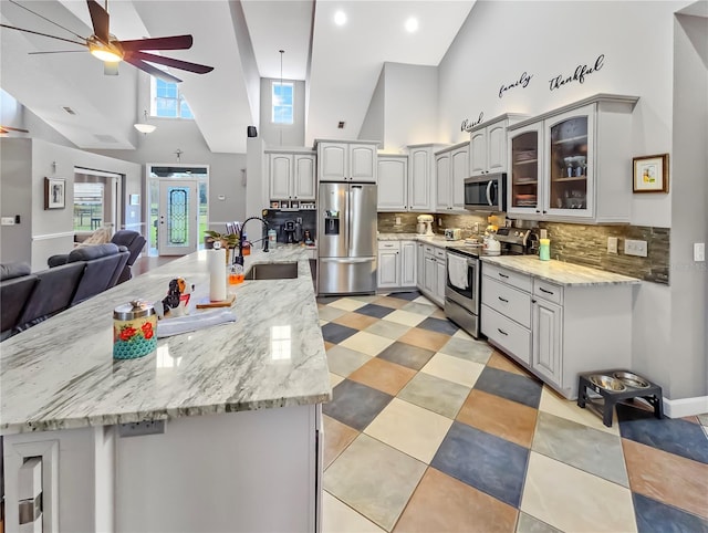 kitchen with stainless steel appliances, a sink, a ceiling fan, open floor plan, and glass insert cabinets