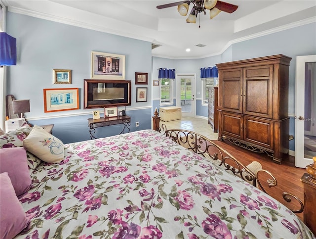 bedroom with visible vents, a raised ceiling, crown molding, and wood finished floors