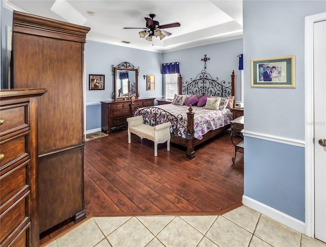 tiled bedroom featuring ceiling fan, visible vents, a raised ceiling, and baseboards