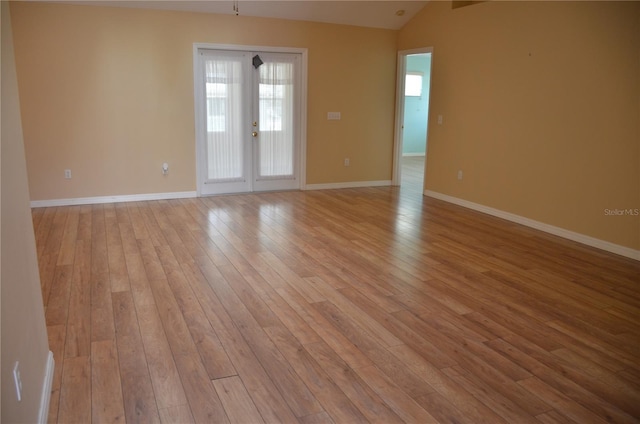 empty room featuring lofted ceiling, baseboards, and light wood-style floors