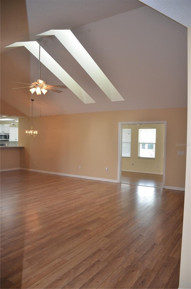 unfurnished living room with ceiling fan with notable chandelier, a skylight, baseboards, and light wood-style floors