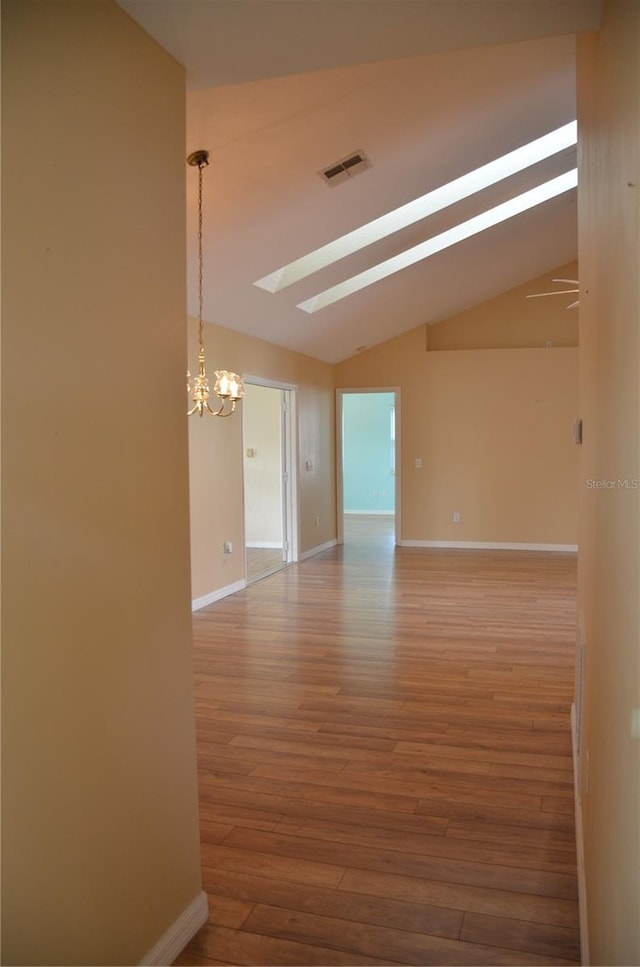 spare room with baseboards, vaulted ceiling with skylight, visible vents, and wood finished floors