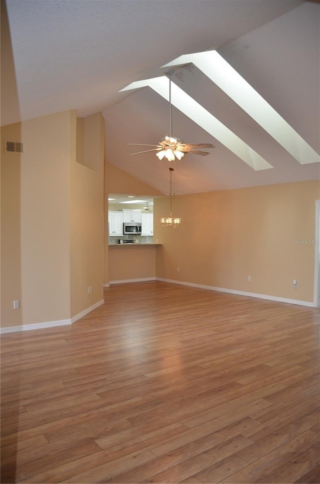 unfurnished living room featuring ceiling fan with notable chandelier, light wood-style flooring, a skylight, and visible vents