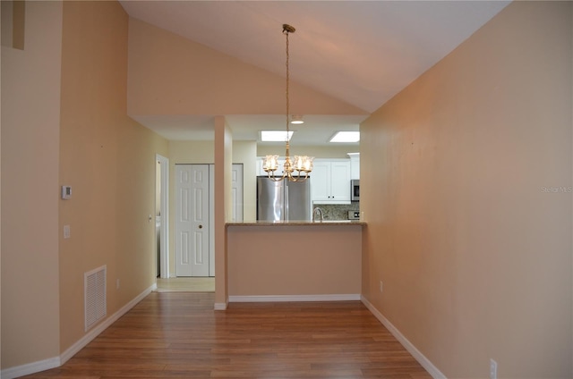 interior space with a chandelier, wood finished floors, visible vents, baseboards, and vaulted ceiling