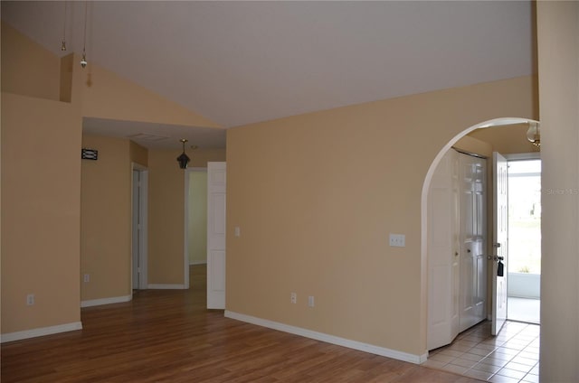 unfurnished room with arched walkways, vaulted ceiling, wood finished floors, and baseboards