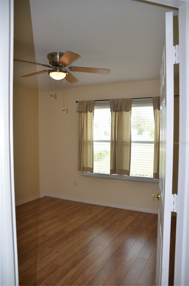 empty room featuring wood finished floors, a ceiling fan, and baseboards