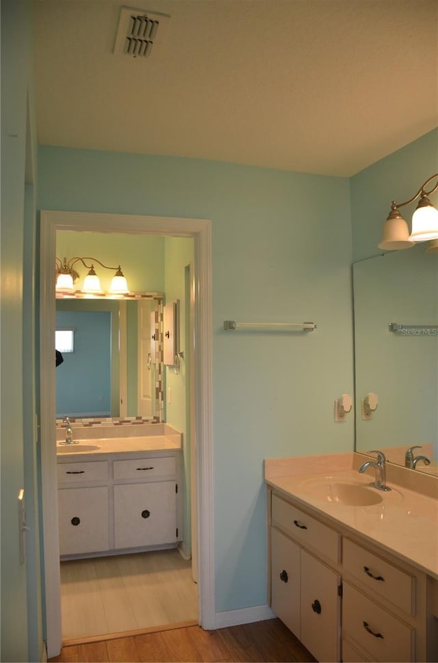 bathroom featuring wood finished floors, two vanities, a sink, and visible vents