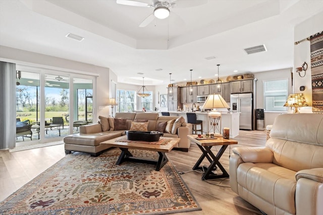 living room featuring a ceiling fan, a tray ceiling, visible vents, and light wood finished floors