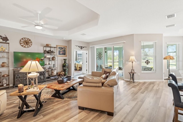 living room with a tray ceiling, a healthy amount of sunlight, and light wood-style flooring