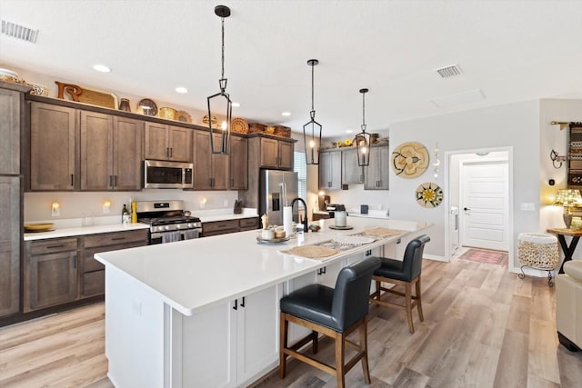 kitchen featuring stainless steel appliances, a kitchen island with sink, light wood-style floors, and visible vents