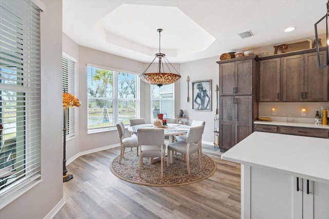 dining space with light wood-style floors, baseboards, visible vents, and a raised ceiling