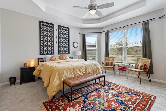 bedroom featuring light carpet, baseboards, a raised ceiling, and a ceiling fan