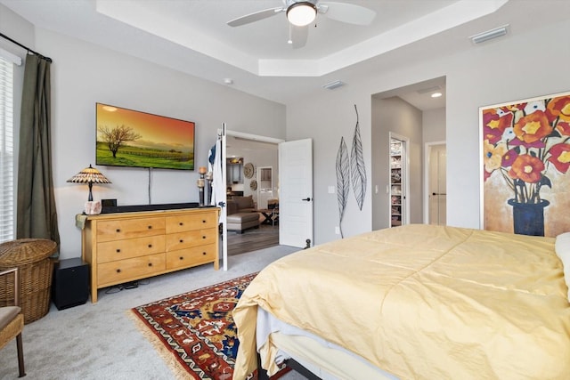 bedroom featuring a tray ceiling, visible vents, ceiling fan, and carpet