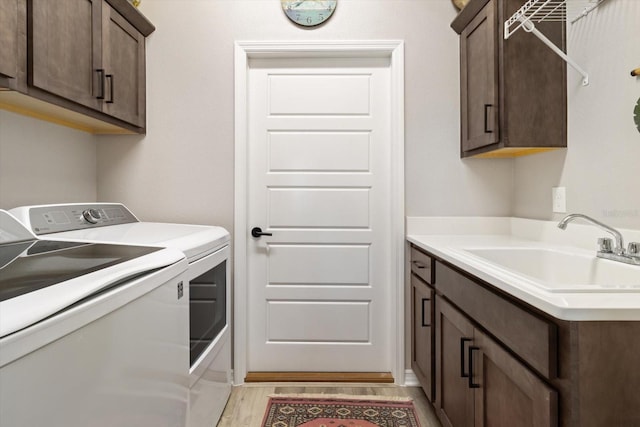 clothes washing area with cabinet space, washing machine and dryer, light wood-style floors, and a sink