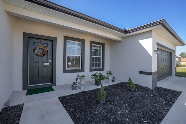 entrance to property with concrete driveway, an attached garage, and stucco siding