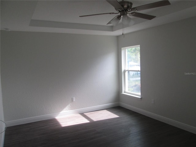 unfurnished room featuring baseboards, a ceiling fan, dark wood-type flooring, and a raised ceiling