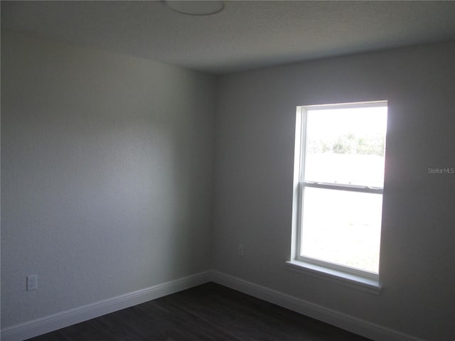 spare room with baseboards, a wealth of natural light, and dark wood-style floors