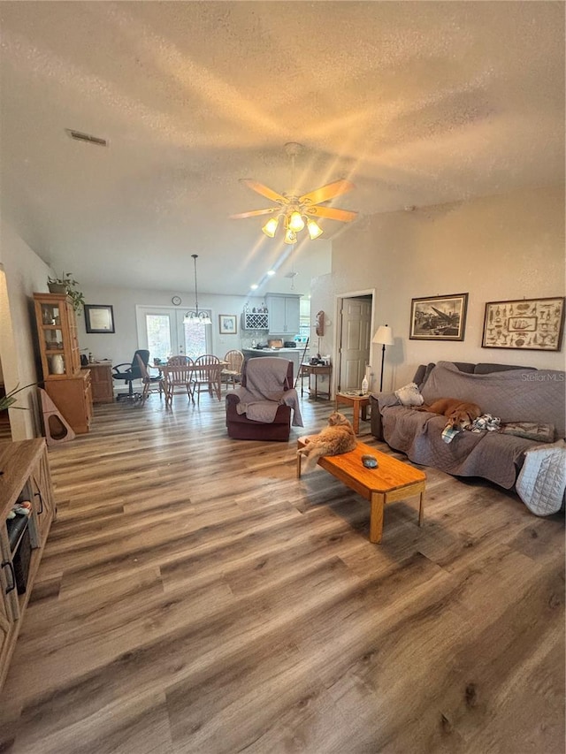 living room featuring lofted ceiling, a textured ceiling, wood finished floors, and ceiling fan with notable chandelier