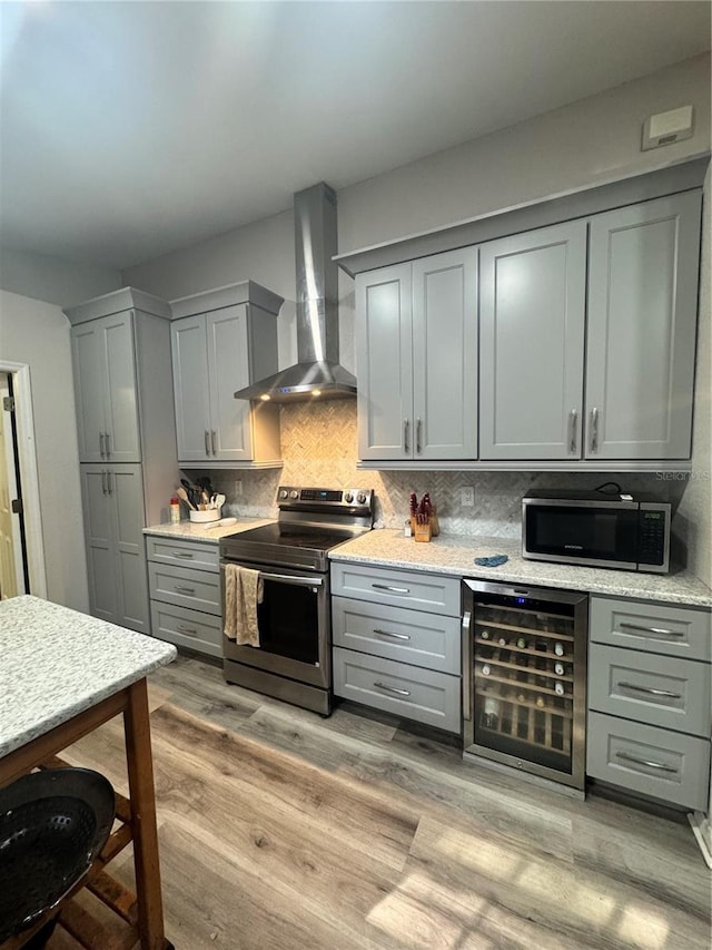 kitchen featuring beverage cooler, stainless steel appliances, gray cabinets, decorative backsplash, and wall chimney exhaust hood