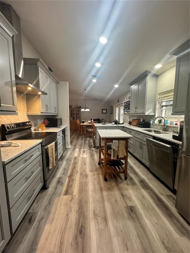 kitchen featuring light wood finished floors, stainless steel appliances, backsplash, gray cabinetry, and a sink