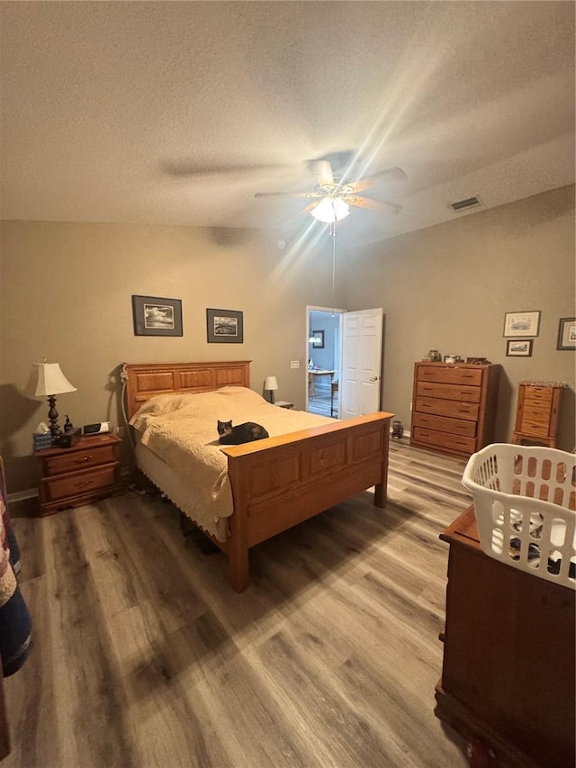 bedroom with a textured ceiling, wood finished floors, visible vents, and a ceiling fan