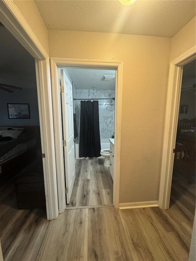 corridor with a textured ceiling, baseboards, wood finished floors, and a textured wall