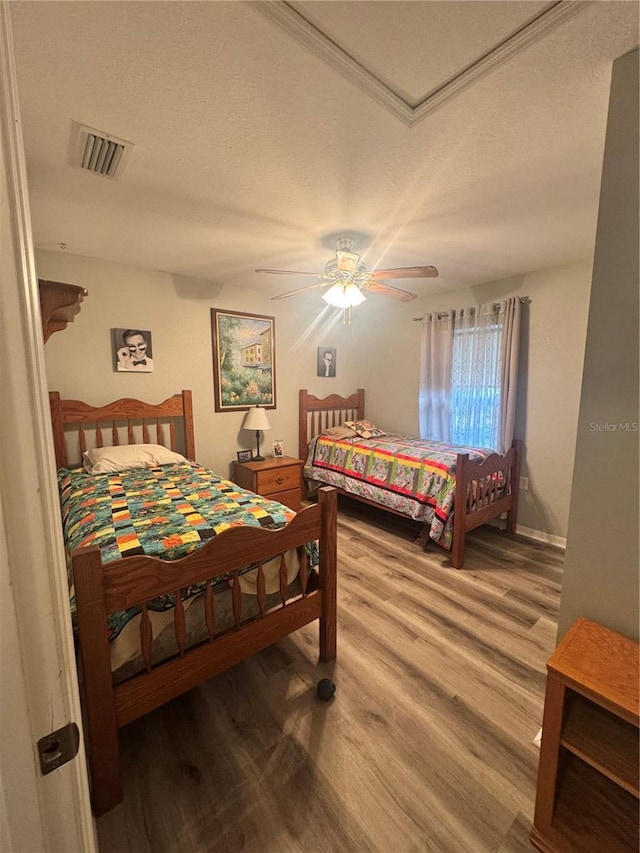 bedroom with ceiling fan, a textured ceiling, visible vents, and wood finished floors