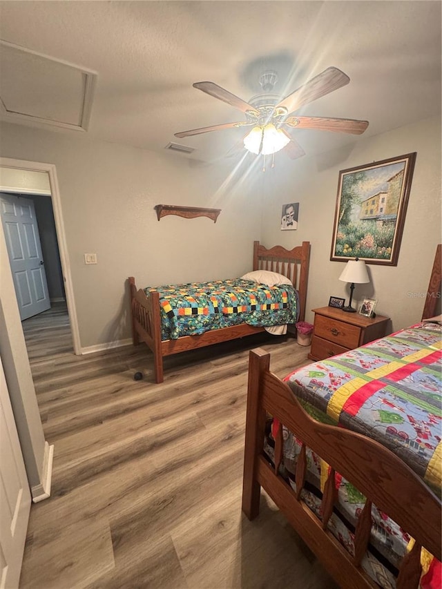 bedroom with attic access, visible vents, baseboards, a ceiling fan, and wood finished floors