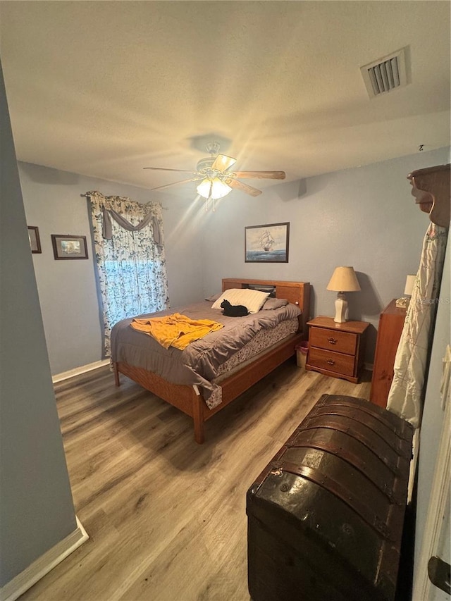 bedroom with light wood-style floors, visible vents, and a ceiling fan