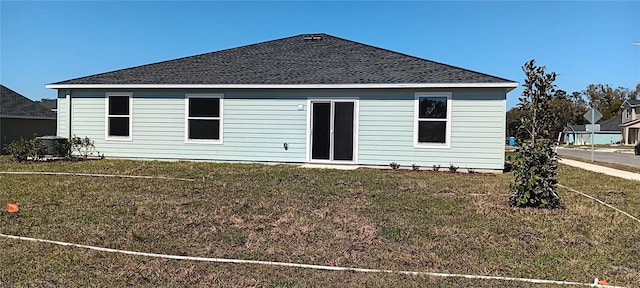 back of house featuring roof with shingles and a lawn