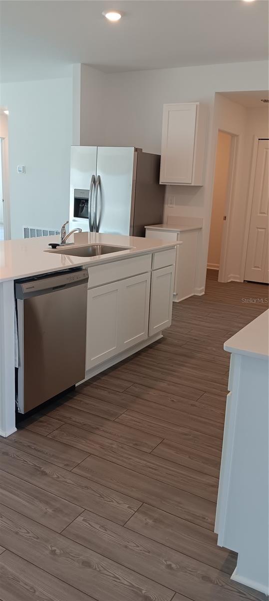 kitchen featuring dark wood-type flooring, a sink, white cabinetry, light countertops, and appliances with stainless steel finishes