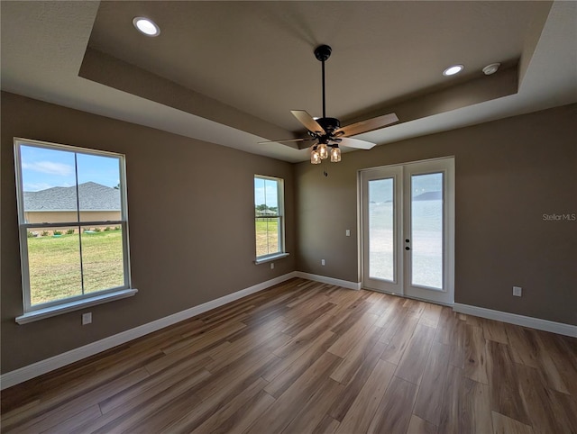 spare room with baseboards, wood finished floors, and a tray ceiling