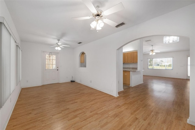 unfurnished living room with light wood finished floors, visible vents, arched walkways, and ceiling fan