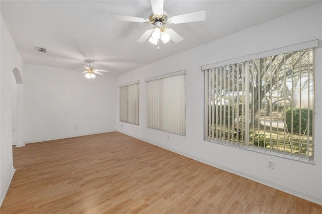 spare room featuring plenty of natural light, arched walkways, visible vents, and light wood-type flooring