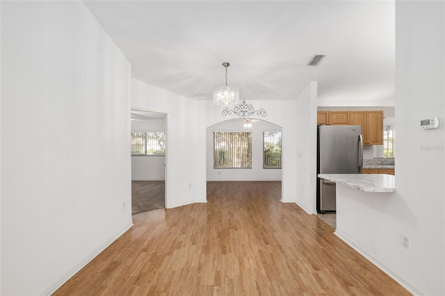 unfurnished dining area featuring baseboards, visible vents, light wood finished floors, arched walkways, and a chandelier