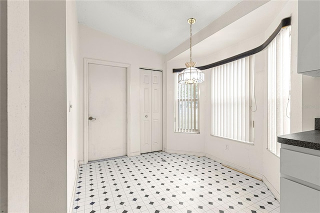 unfurnished dining area featuring lofted ceiling, light floors, baseboards, and an inviting chandelier