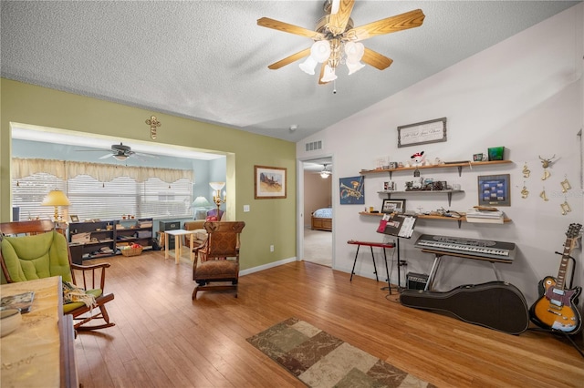 living area with lofted ceiling, a textured ceiling, wood finished floors, visible vents, and a ceiling fan