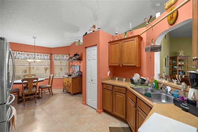 kitchen featuring brown cabinetry, decorative light fixtures, freestanding refrigerator, light countertops, and a sink