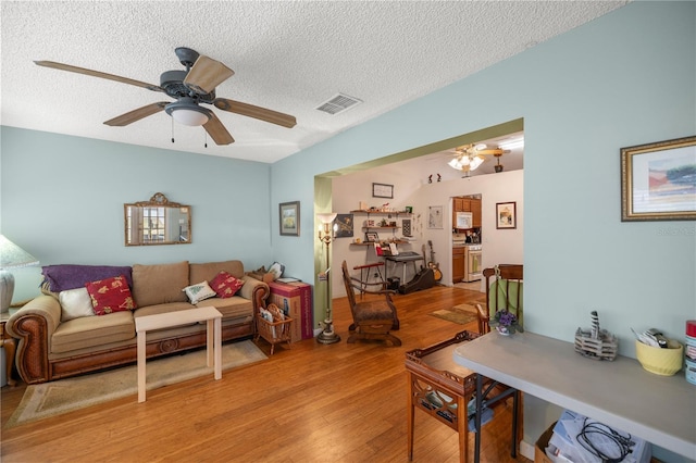 living room with light wood-style floors, visible vents, ceiling fan, and a textured ceiling