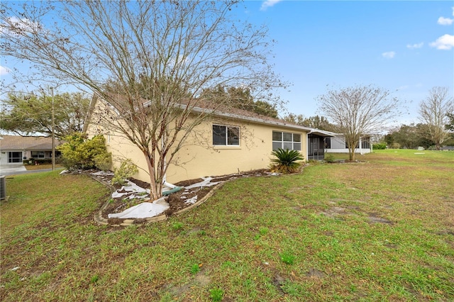 view of side of property featuring a yard, central air condition unit, a sunroom, and stucco siding